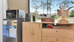 Een kitchenette met een magnetron, een koffiezetapparaat en een bordje met thee op een houten kast.