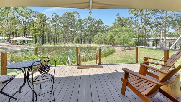 Une terrasse en bois avec une table et des chaises, donnant sur un étang et des arbres.