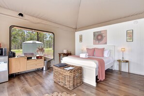 Un dormitorio con cama, escritorio, cesto de basura y vistas al exterior.