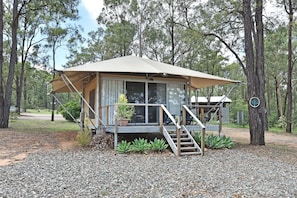 A small, single-story cabin with a covered porch, surrounded by trees.