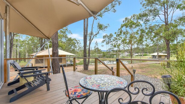 A covered outdoor seating area with a table and chairs, overlooking a natural landscape with trees and a body of water.