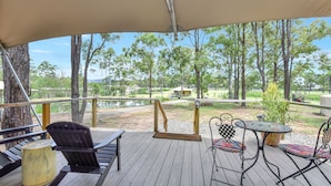 A wooden deck with outdoor furniture, including chairs and a table, overlooking a natural landscape with trees and a body of water.