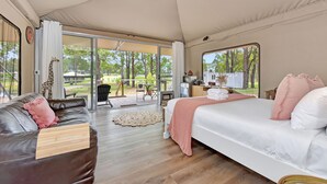 A tent-style room with a bed, a sofa, a dining area, and a view of the outdoors.