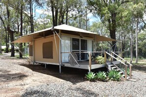 A single-story, open-sided structure with a covered porch, a set of stairs leading to a door, and a gravel ground.
