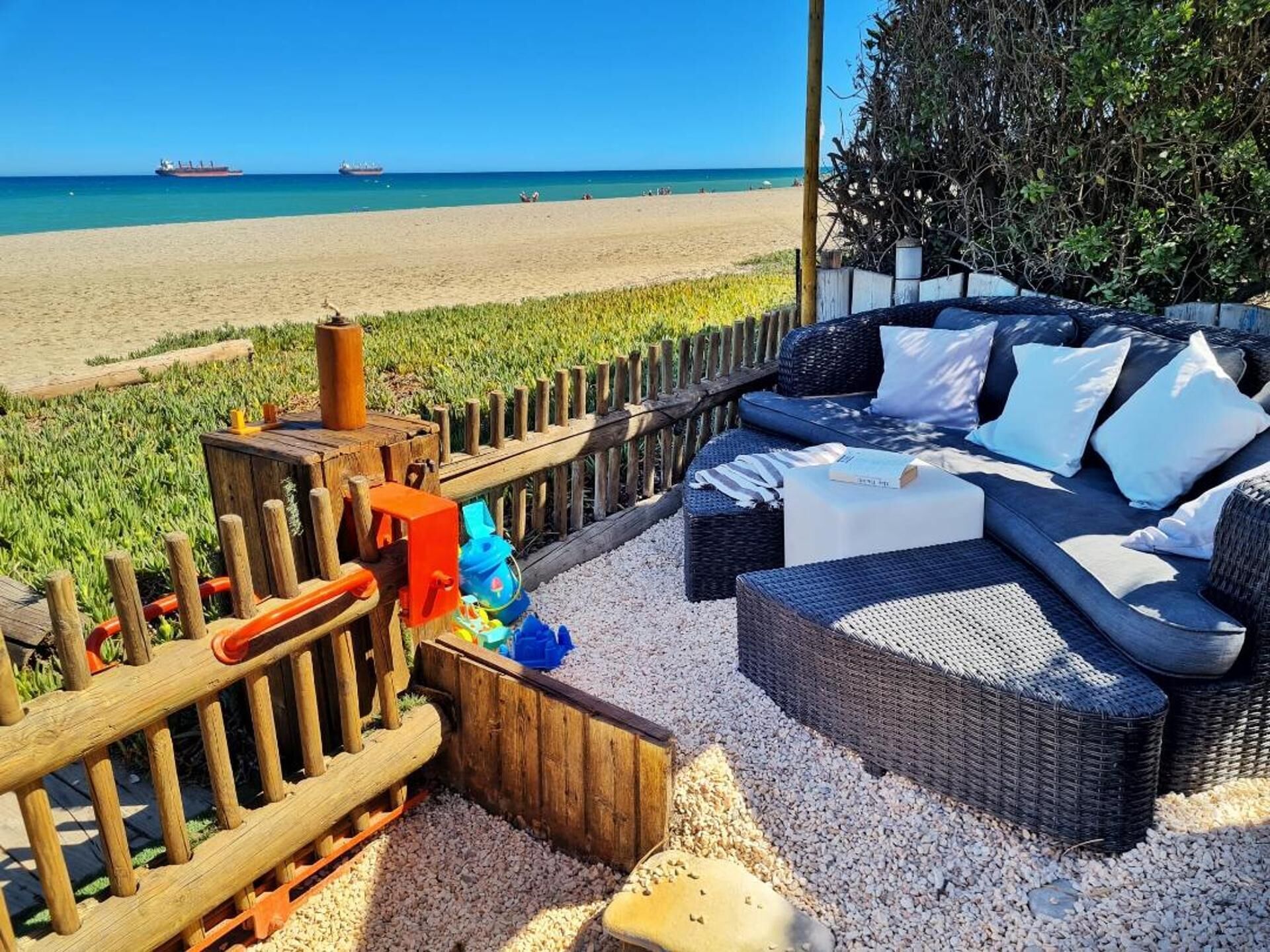 A beachside seating area with wicker furniture and a wooden fence.