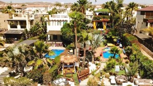 Ein Resort mit mehreren Schwimmbecken, Palmen und einem Gebäude mit einem Reetdach.