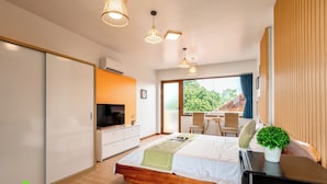 A modern bedroom with a bed, bedside table, TV, and a view of greenery outside. - Room in House - Trang An Ao Dai Homestay - Double Room With Field View - Tam Coc Room (Hoa Lu)