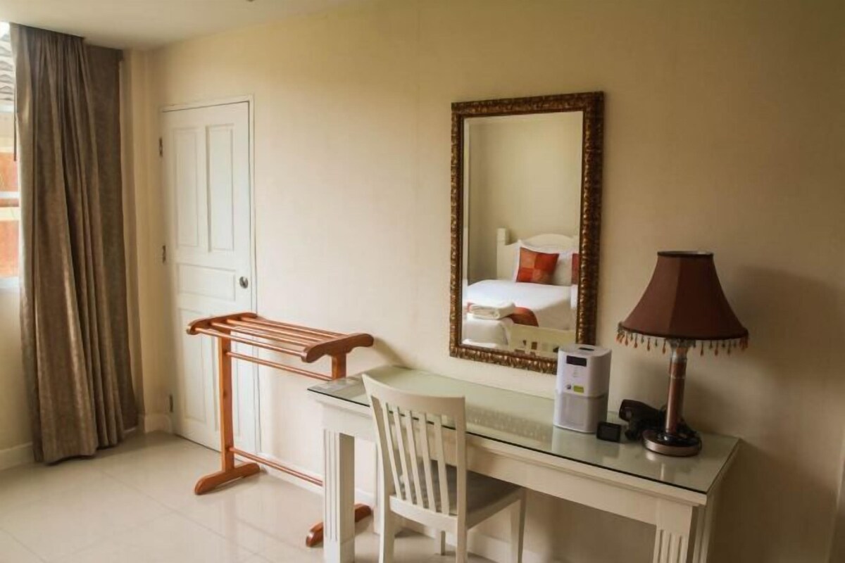 A hotel room with a desk, chair, mirror, lamp, and a window with curtains.