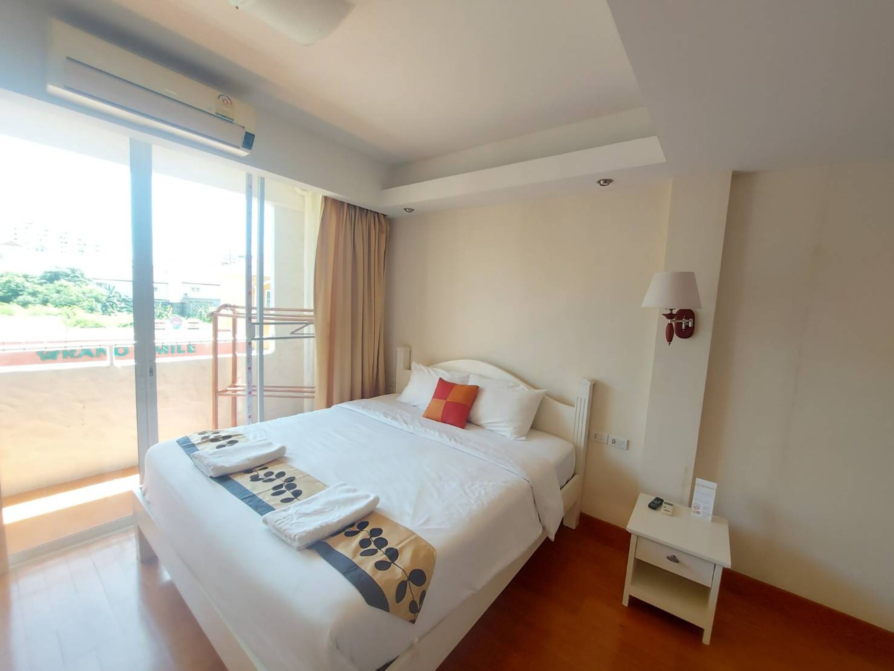A hotel room with a large bed, a nightstand, a lamp, and a view of a cityscape through the window.