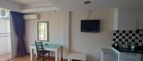 Um espaço de estar compacto com área de jantar, uma kitchenette pequena e uma televisão na parede.