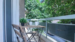 Een balkon met een houten tafel, twee witte bekers, een potplant en een metalen tralie.
