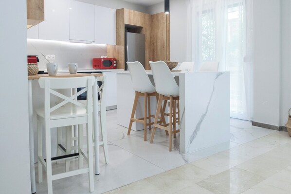 Une cuisine moderne avec des meubles blancs, un îlot central en bois et des tabourets de bar.