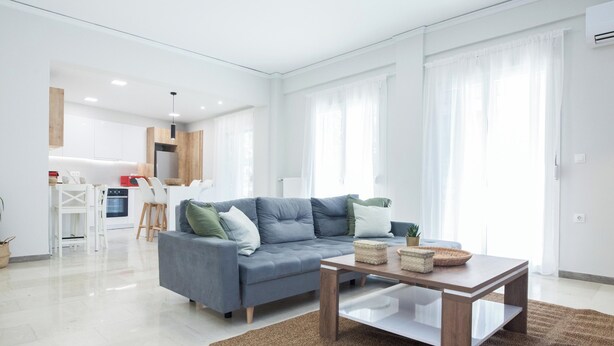 Een moderne woonkamer met een grijze bank, een houten salontafel en een keuken op de achtergrond.