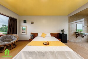 Een slaapkamer met een groot bed, een houten hoofdbord, een nachtkastje met een plant en uitzicht op de omgeving door een raam.