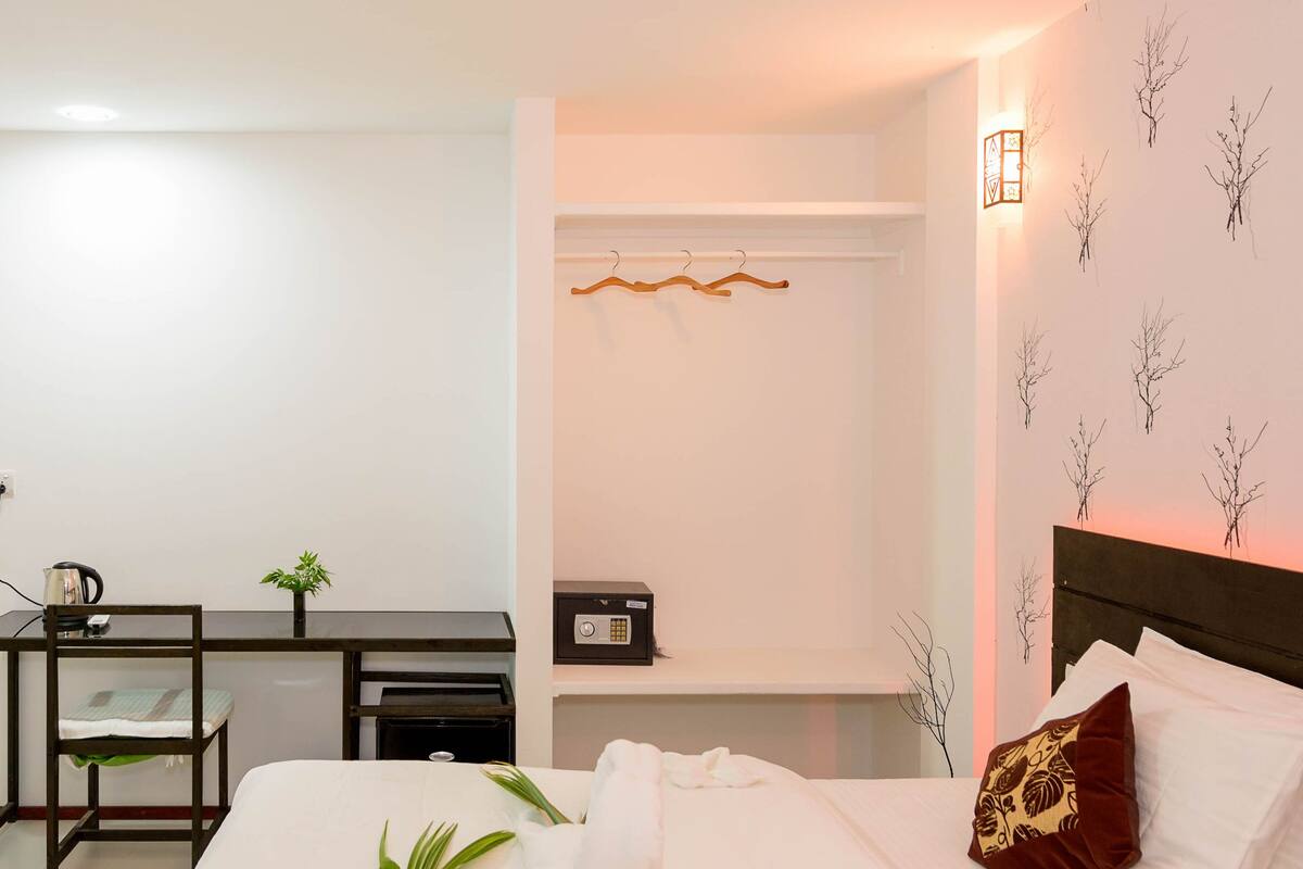 Hotelkamer met een bed, een bureau, een stoel, een klein tafeltje, een plant en een wandlamp.