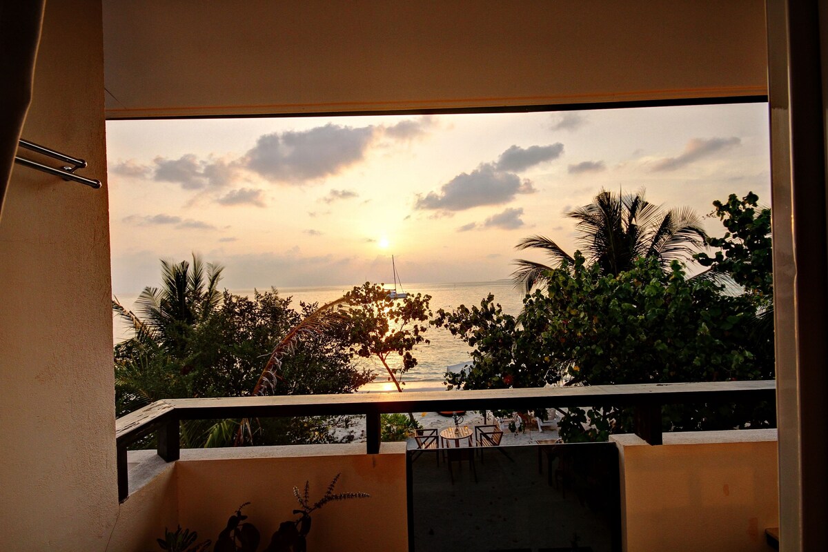 Een balkon met uitzicht op een zonsondergang boven de zee, omringd door groen.