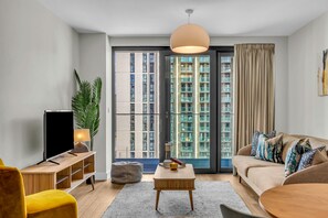 Un salon moderne avec un canapé, une table basse, un téléviseur et une grande fenêtre avec des rideaux.