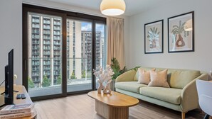 A modern living room with a sofa, a coffee table, and a TV. - Vibrant One Bed Apartment in Wembly by MySquare (Wembley Park)