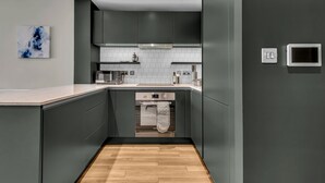A modern kitchen with dark cabinets, a built-in oven, and a white tiled backsplash. - Vibrant One Bed Apartment in Wembly by MySquare (Wembley Park)