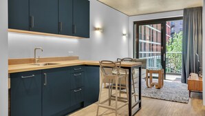 A modern kitchen with dark cabinets, a wooden countertop, and a bar stool. - Vibrant One Bed Apartment in Wembly by MySquare (Wembley Park)