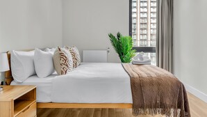 A neatly made bed with white and patterned pillows, a brown throw blanket, and a green plant beside it. - Vibrant One Bed Apartment in Wembly by MySquare (Wembley Park)