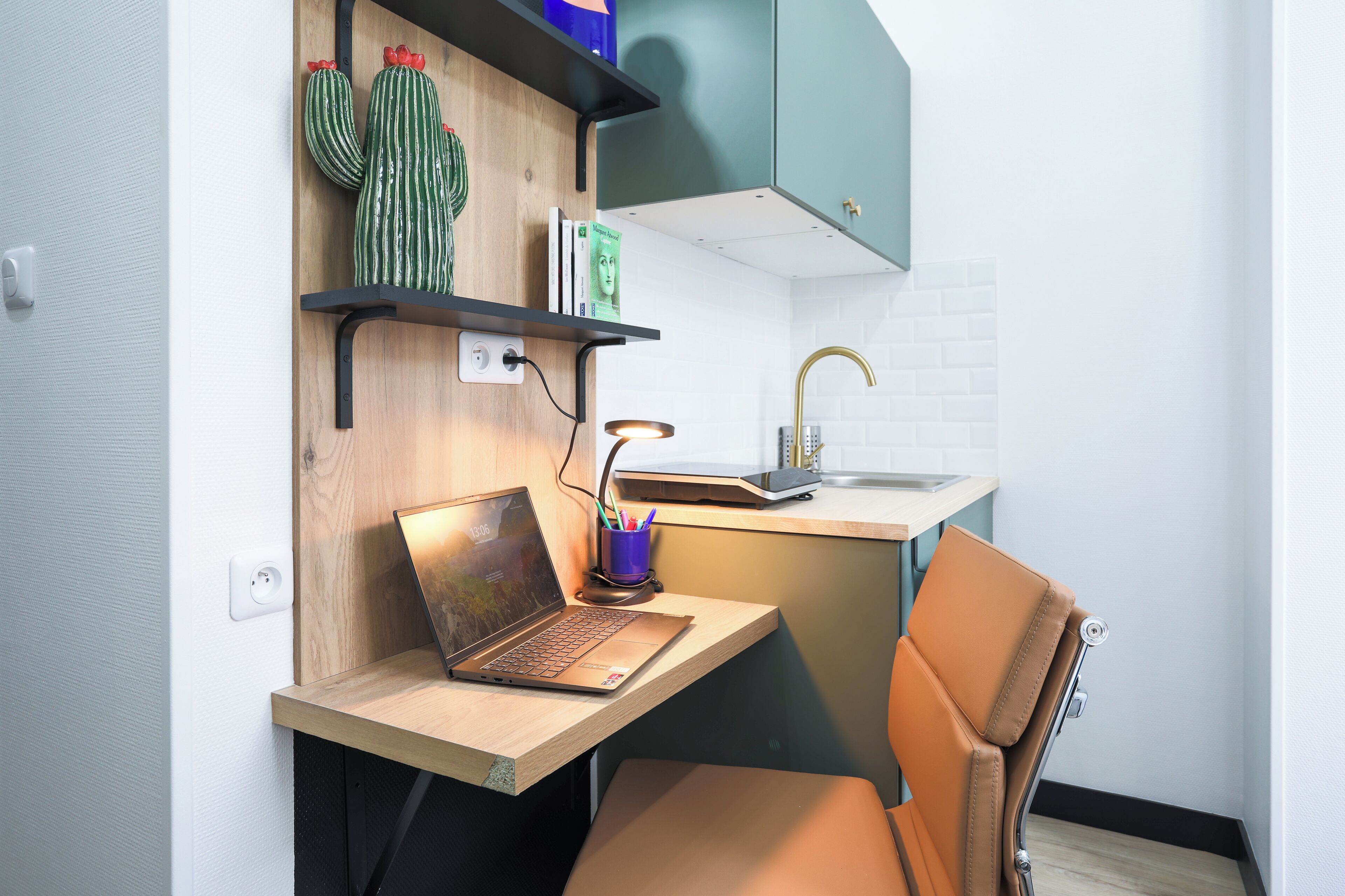 A modern kitchen with a wooden countertop, a laptop, a chair, and a cactus decoration.
