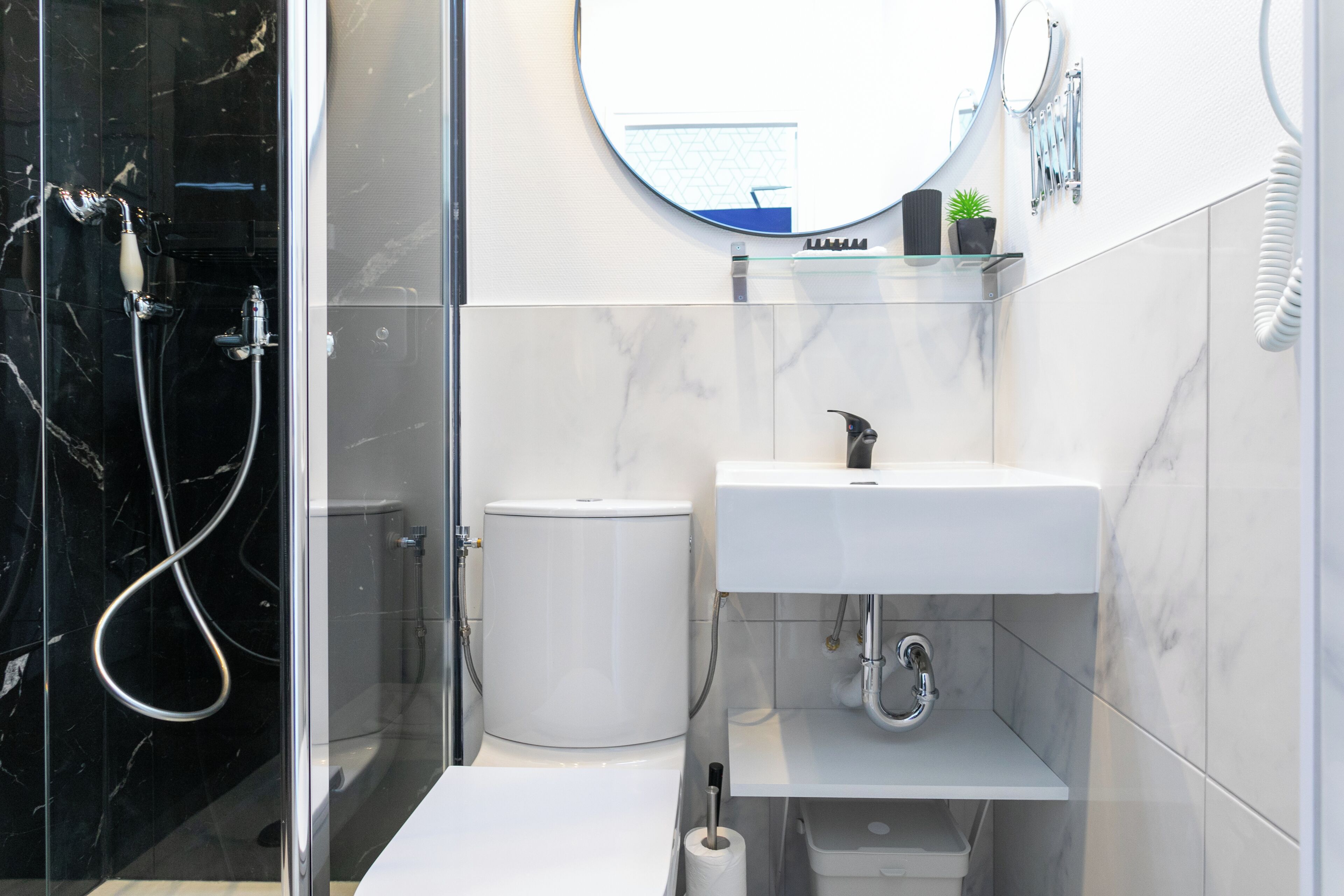 A modern bathroom with a glass shower enclosure, a white toilet, a sink with a mirror above it, and a small shelf with toiletries.