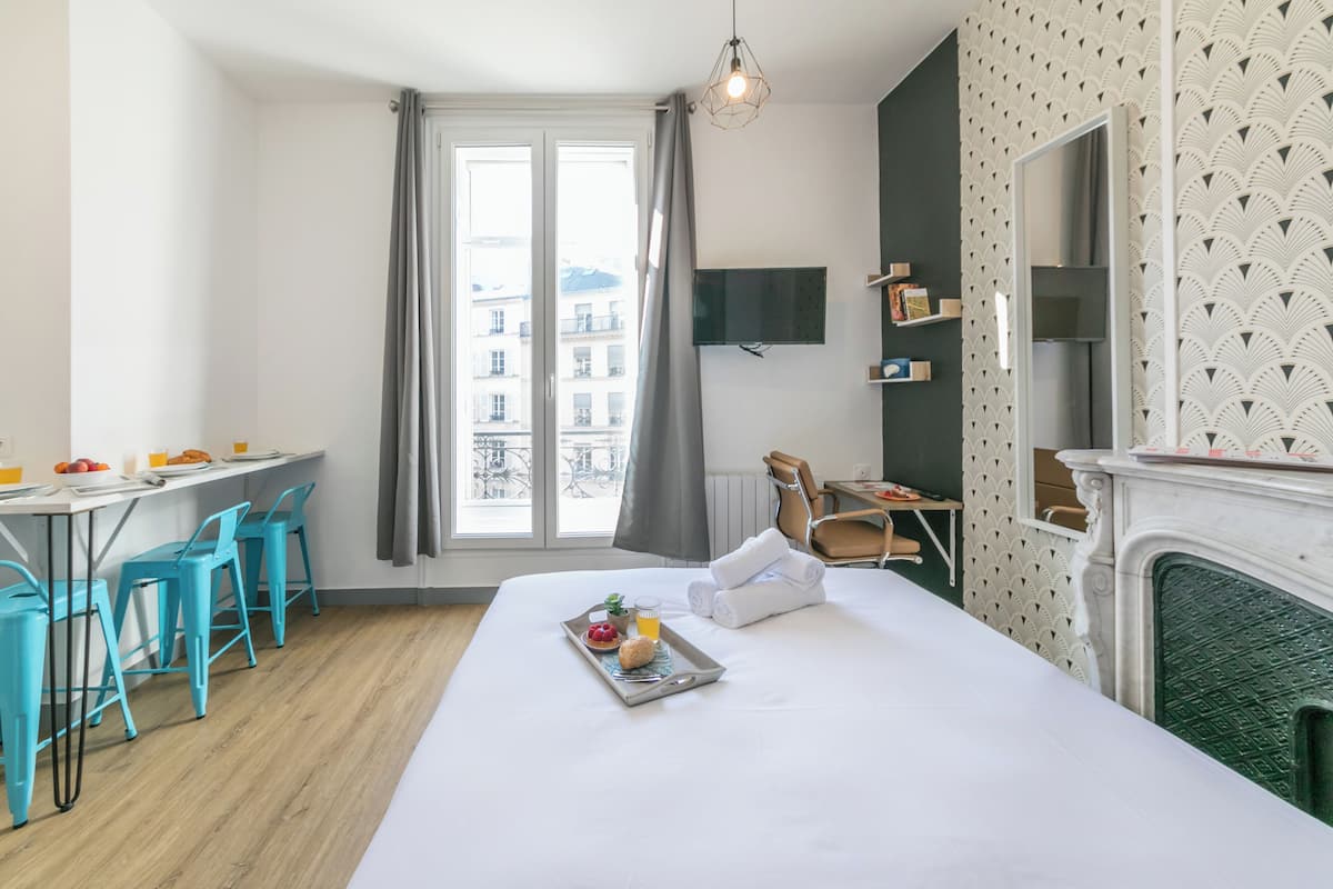 A modern hotel room with a bed, a dining area with chairs, a TV, and a fireplace.
