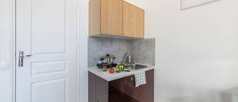 Una cocina compacta con una puerta blanca, un mueble de madera, un fregadero y una encimera con una olla, un hervidor y algunas verduras.