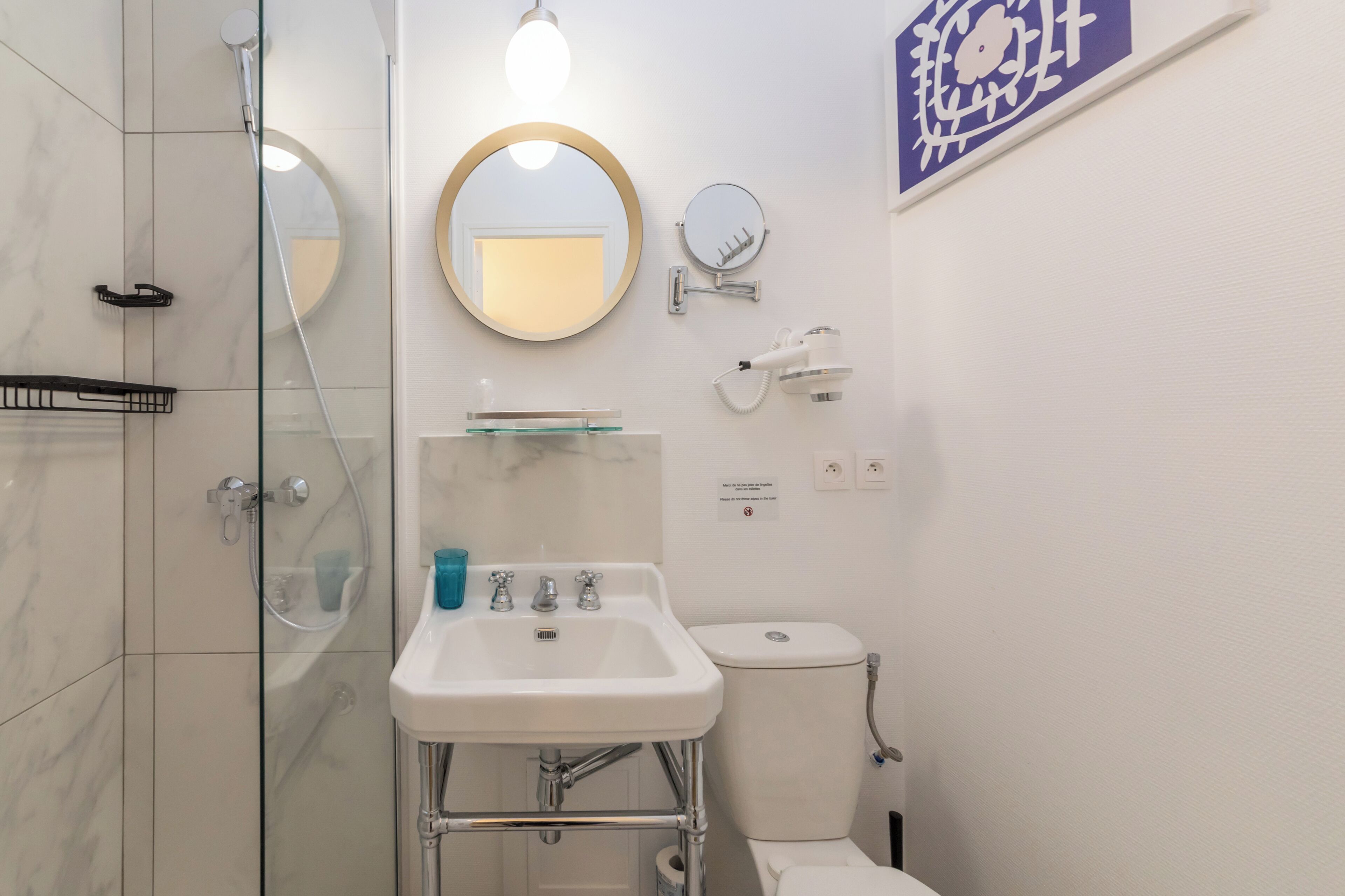 A bathroom with a glass shower enclosure, a white sink with chrome fixtures, a toilet, and a wall-mounted mirror.