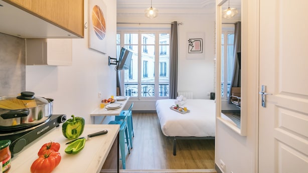 Een compacte hotelkamer met kitchenette, een eethoek en een bed.