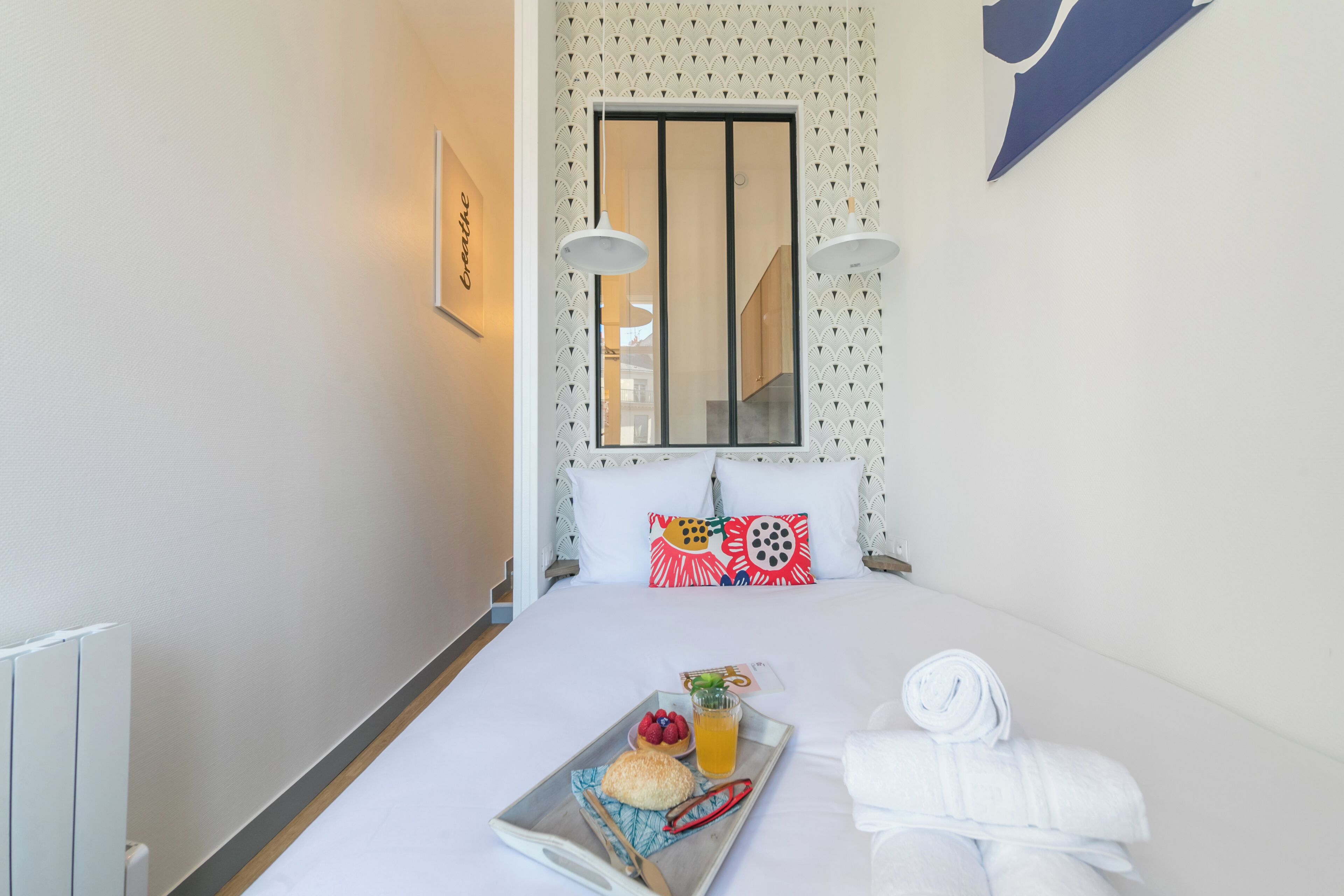 A hotel room with a bed, a tray with food, a window, and a wall with a pattern.