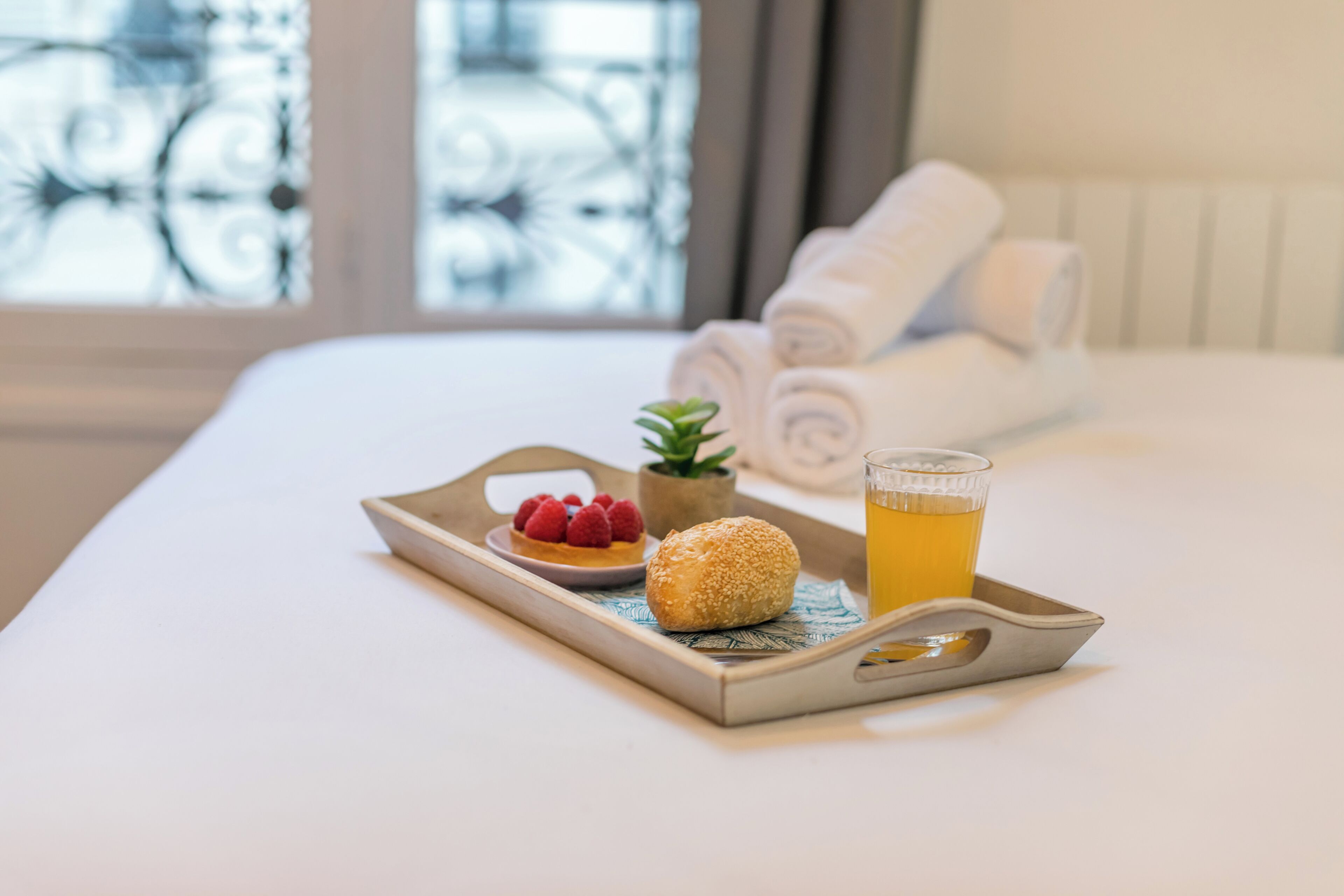A tray with a pastry, a glass of juice, and a small plant on a bed.