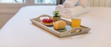 A tray with a pastry, a glass of juice, and a small plant on a bed.