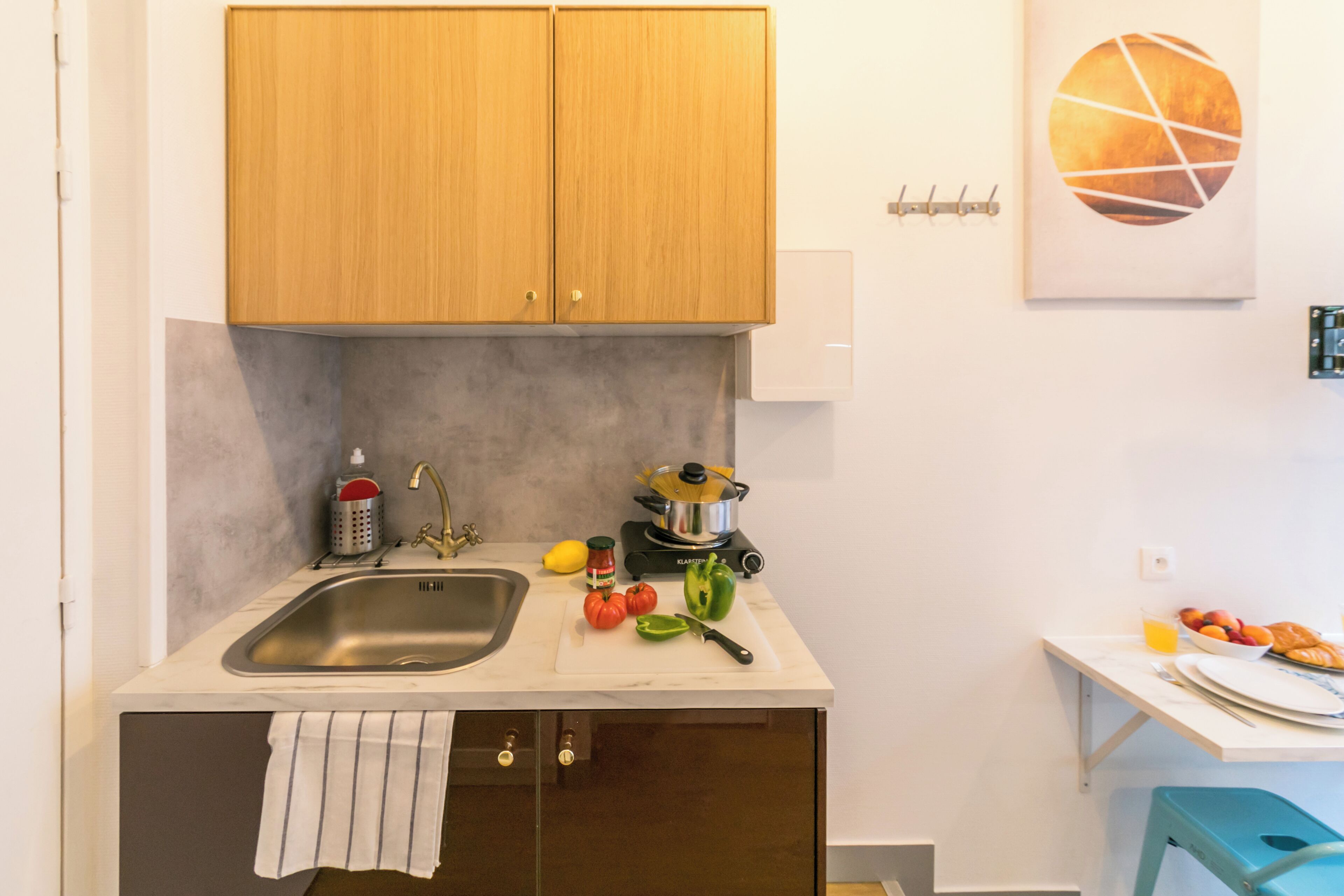 Une cuisine avec des meubles de rangement en bois, un évier, une cuisinière et un plan de travail sur lequel on trouve des légumes et une planche à découper.