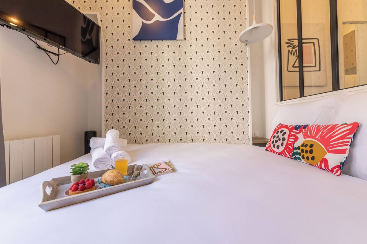 A neatly made bed with a tray of breakfast items, a pillow with a floral pattern, and a wall with a geometric design.