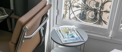 A waiting area with a chair, a small table with a magazine, and a window with decorative iron bars.
