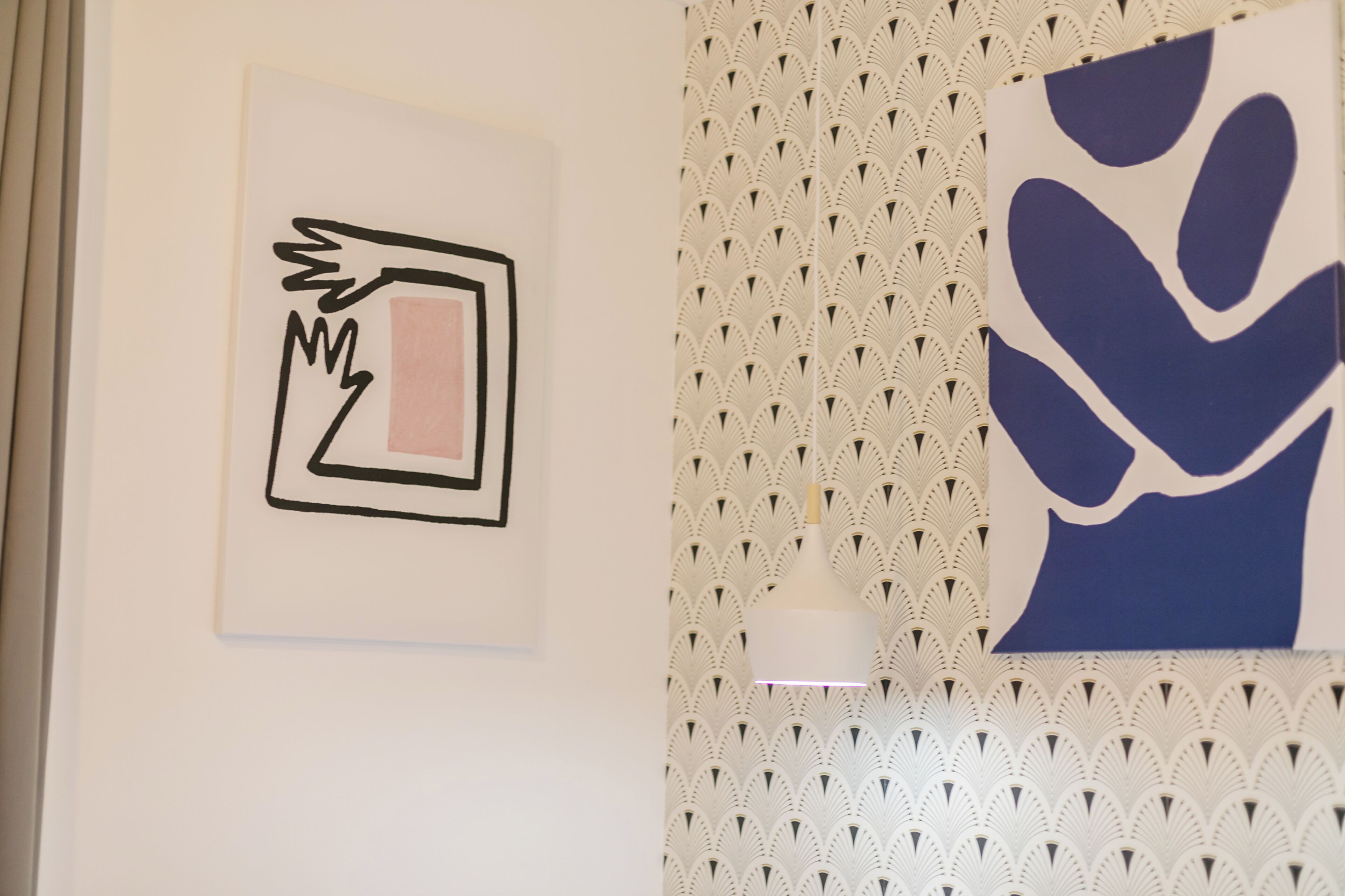 Una parete con due opere d'arte appese, una astratta e una raffigurante un gesto della mano, e una carta da parati decorata.