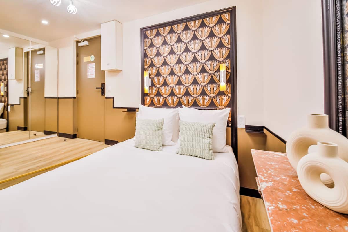A hotel room with a large bed, a wooden headboard with a patterned design, a marble side table, and a large mirror.