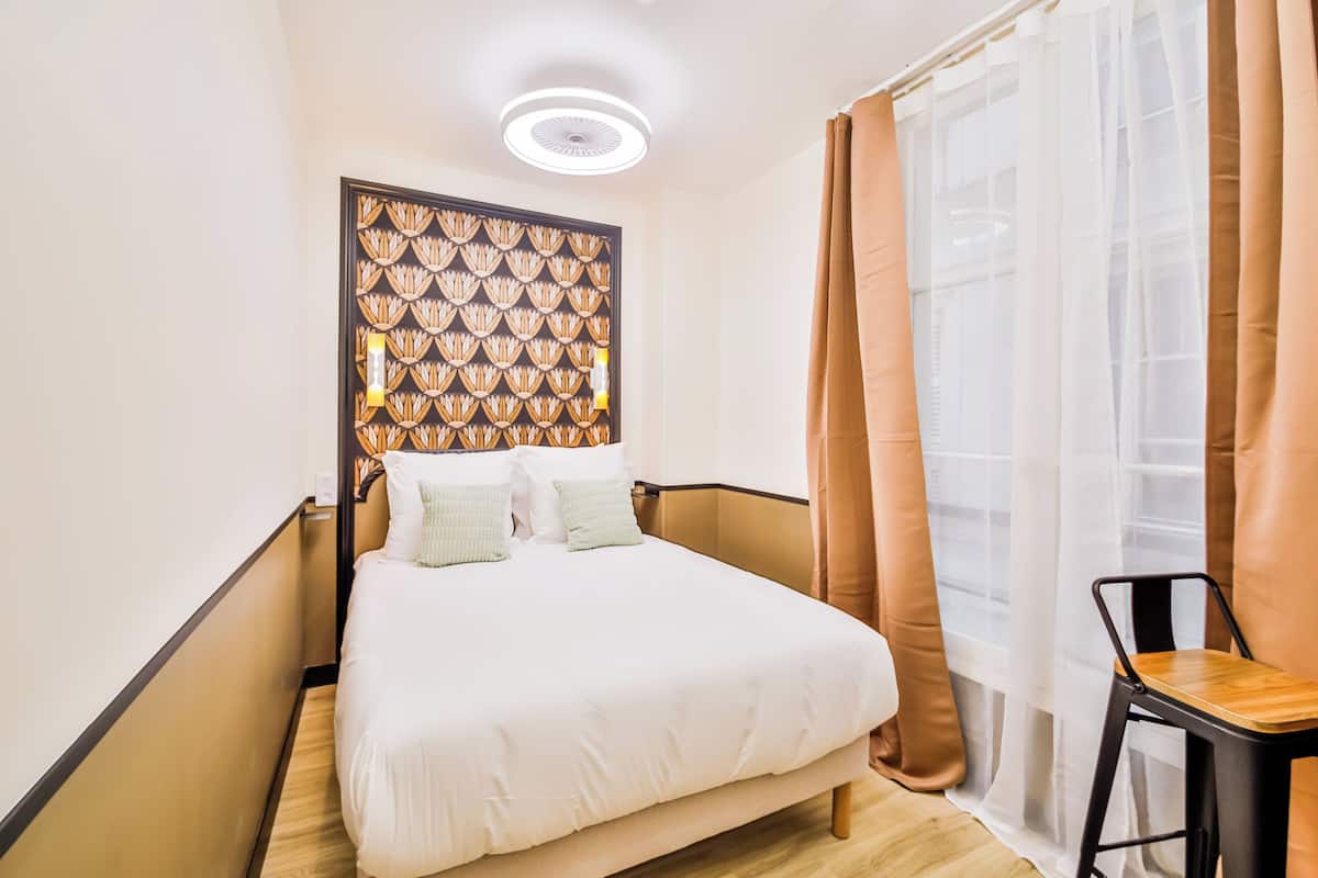 A neatly arranged hotel room with a bed, a chair, and a window with curtains.