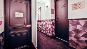 A hotel corridor with a 'Sortie / Exit' sign on a door, directional signs on the walls, and geometric patterned walls. - WS Louvre - Saint-Florentin (Paris)