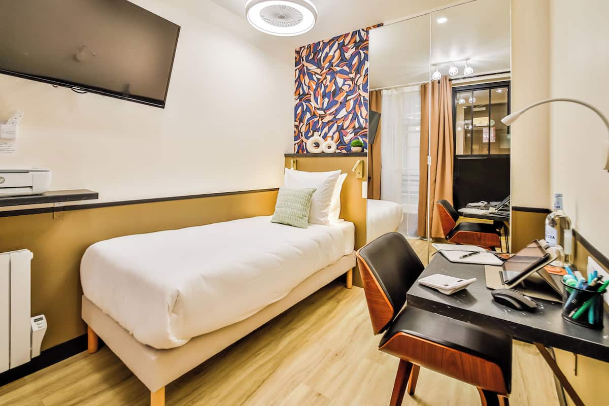 A hotel room with a bed, desk, chair, and a TV mounted on the wall.