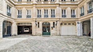 A courtyard with cobblestone flooring, a central entrance with a green door, and a white garage door. - WS Louvre - Saint-Florentin (Paris)