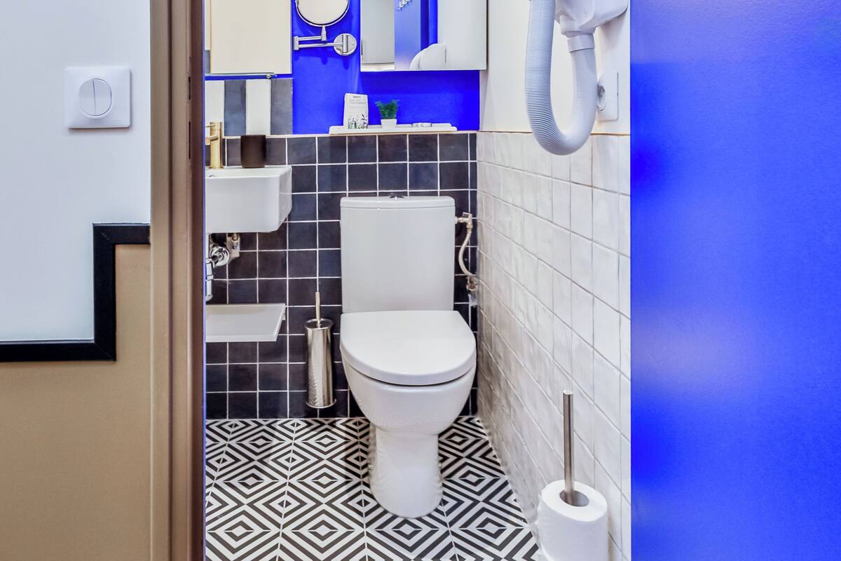 A modern bathroom with a geometric patterned floor, a white toilet, a sink with a mirror, and a hairdryer mounted on the wall.