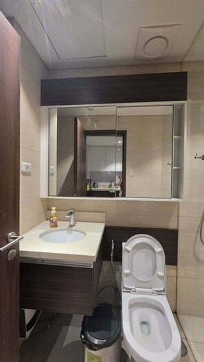 Un baño con lavamanos, espejo, inodoro y un cubo de basura.