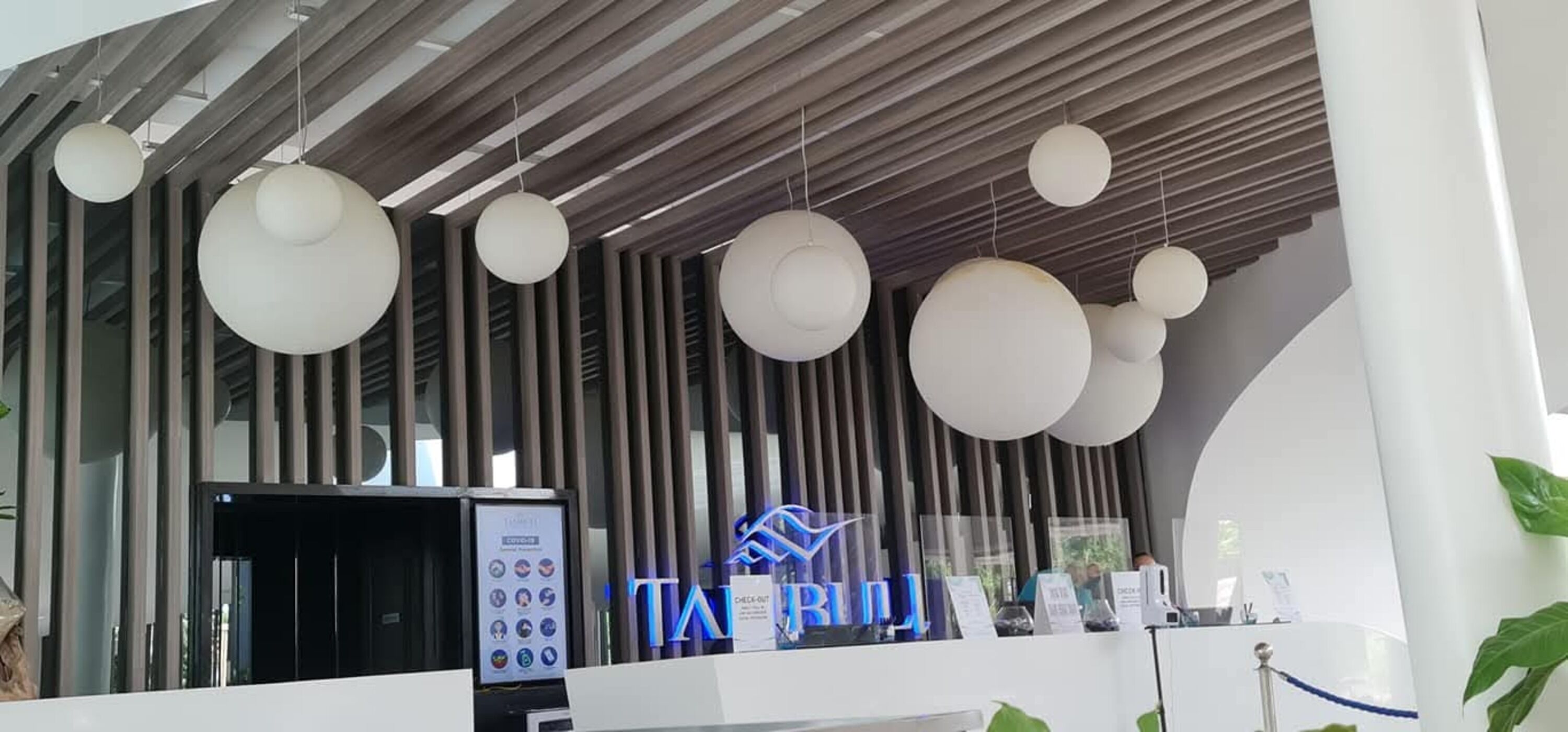 A reception area with a modern design, including a check-in kiosk, a reception desk, and a logo with a blue and white color scheme.