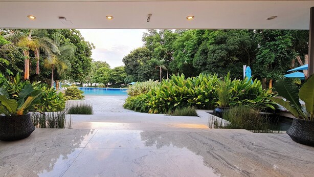L'ingresso moderno di un hotel con piscina, immerso nel verde e circondato da piante in vaso.
