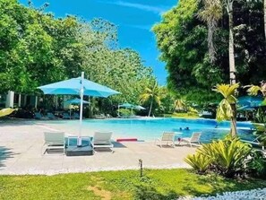 A pool area with lounge chairs and umbrellas, surrounded by lush greenery. - Tambuli Tower C Unit 5D (Lapu-Lapu)