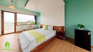 A bedroom with a bed, a small desk, a chair, a window with a view, and a refrigerator. - Room in House - Trang An Ao Dai Homestay - Double Room With Field View - Hang Mua Room (Hoa Lu)