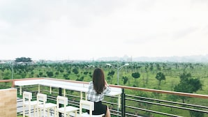 A woman sitting on a balcony with a view of a green field and distant buildings. - Room in House - Trang An Ao Dai Homestay - Double Room With Field View - Hang Mua Room (Hoa Lu)